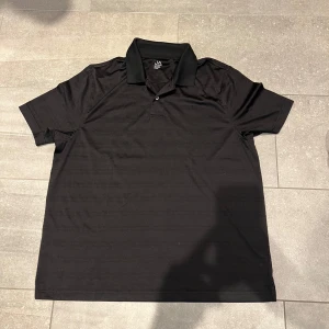 Svart pikétröja - Klassisk svart pikétröja med krage och två knappar framtill. Tröjan är av ett tunt mönstrat material, relaxed fit. Perfekt för dig som gillar luftigare plagg.