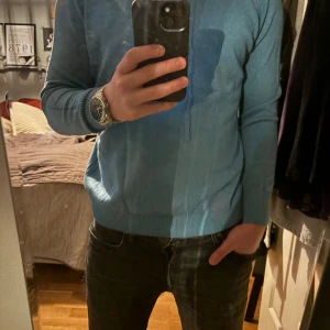 Ljusblå stickad hoodie - Säljer en ljusblå stickad hoodie med huva och dragsnören. Tröjan har lång ärm och ribbade muddar vid ärmslut och nederkant. Perfekt för en avslappnad stil och passar bra till jeans.