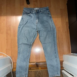 Ljusblå mom jeans från Stradivarius - Säljer ett par ljusblå mom jeans från Stradivarius med hög midja och slim passform. Klassisk femficksmodell med dragkedja och knapp framtill. Perfekta till vardags för en avslappnad men trendig look.