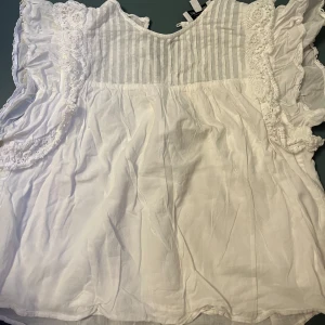 Vit blus med spetsdetaljer från & other stories - Söt vit blus med volangprydda ärmar och spetsdetaljer längs axlarna. Blusen har en lös passform och är tillverkad i ett lätt bomullstyg. Perfekt för vår och sommar!🤍