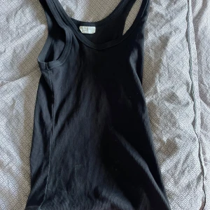 Svart ribbad linnetopp  - Svart ribbad linnetopp från Gina Tricot i storlek S. Toppen har en klassisk rund halsringning och ärmlös design med breda axelband.  Materialet är mjukt och stretchigt.