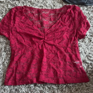 Röd spetsblus från SHEIN - Snygg röd blus från SHEIN i storlek S, med transparent spetsmaterial och v-ringad hals. Blusen har korta ärmar och en cool rynkdetalj framtill som ger extra stilpoäng. Perfekt för dig som gillar att sticka ut med färg och detaljer.