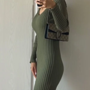 Olivgrön ribbad långklänning - Snygg olivgrön långklänning med ribbad struktur och figurnära passform. Klänningen har v-ringad hals och långa ärmar, vilket ger en stilren och modern look. Perfekt för dig som gillar enkel men trendig design.