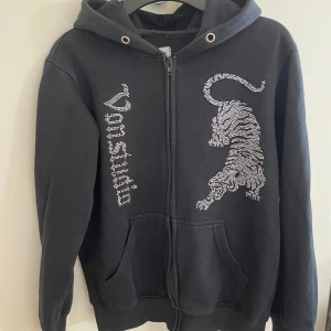 Svart hoodie från vonstudio - En svart hoodie men vita glittriga prickar som blir en tiger och med namnet på framsidan, inga snören. Modellen är 165cm och väger 49kg och storlek xs. Ny pris: 800 mitt pris 400. OBS! Den är mindre i storleken, hör gärna av er innan ni köper👍🏻