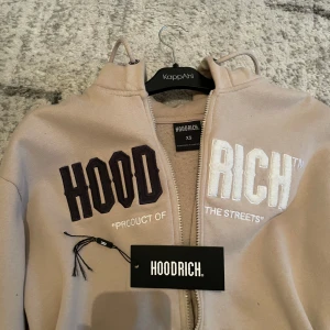Beige hoodie från Hoodrich med dragkedja - Säljer en beige hoodie från Hoodrich i storlek XS men passar mig som använder (M). Tröjan har broderad text i svart och vitt på bröstet, huva med snörning och praktiska fickor framtill. Materialet är mjukt och skönt, perfekt för chill dagar. Dragkedja hela vägen och långärmad modell. Ny pris 800kr mitt pris 400kr 