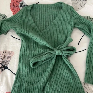 Grön ribbad omlottkofta med knyt - Snygg grön ribbad omlottkofta med v-ringning och långa ärmar. Koftan har ett brett knytband i midjan som ger en cool och figurnära passform. Perfekt att styla med jeans eller kjol för en chill look. Materialet är mjukt och stickat, vilket gör den skön att ha på sig. Priset kan även diskuteras❣️
