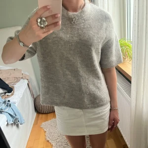 Grå stickad tröja med kort ärm - Säljer en enkel och grå stickad tröja med korta ärmar. Tröjan har rund hals och är ifrån GinaTricot🌸