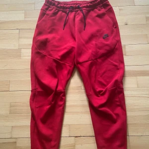Äkta Nike Tech byxor (röda) - Röda äkta Nike Tech Fleece byxor från Nike med svart logga på låret och snörning i midjan. Byxorna har en tapered passform, elastisk midja och dragkedja på ena bakfickan. Perfekta för chill eller träning, tillverkade i mjuk bomullsmix. Säljer då dom aldrig kommer till användning! Endast använd 3 gånger! Kan användas av dam och herr! Ända skavankerna ser ni på 3e och 4e bilden! Köpt för 1149kr som ni ser på sista bilden! Säljer för 950! Vid snabb affär kan priset diskuteras så lägg bud!❣️❣️❣️
