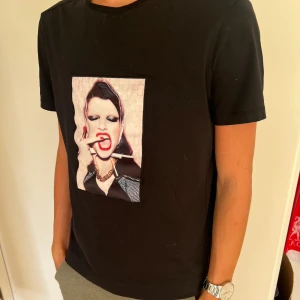 Svart Limitato t-shirt XS med print - Svart t-shirt från Limitato i storlek XS med ett stort konstnärligt print framtill av Ellen Von Unwerth. T-shirten har rund hals och korta ärmar, tillverkad i mjuk bomull. Snygg och unik design som sticker ut med sitt coola motiv. *Nypris 1599kr. T-shirten skickas med originalkartongen 