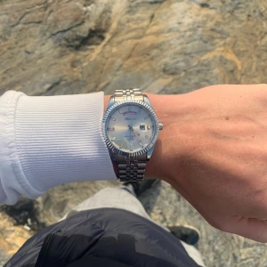 Silverfärgad klocka från Doventi - Stilren klocka från Doventi  med rund urtavla i silver och dag- och datumvisning. Armbandet är i klassisk länkdesign av metall och boetten har räfflad kant. Perfekt för dig som gillar tidlös och clean stil.