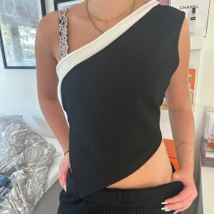 Svart och vit oneshoulder topp från SHEIN - Snygg svart topp med vit kant från SHEIN i oneshoulder-modell. Asymmetrisk form som ger en cool vibe och är tillverkad i mjuk polyester. Perfekt för dig som vill sticka ut med en unik och trendig look. Passar dig som gillar att experimentera med stilar.