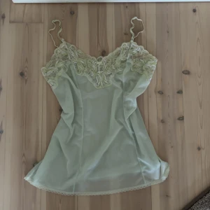 Ljusgrön spetslinnetopp med broderi - Supersöt ljusgrön linnetopp med tunna axelband och detaljerad spetsbroderi i samma ton över bysten. Toppen har en mjuk, flowy passform och är dekorerad med spetskant längst ner. Perfekt för dig som gillar romantiska och feminina vibes.