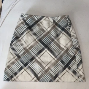 Rutig kortkjol från H&M i beige och blå - Supersnygg kortkjol från H&M i storlek 34 med rutigt mönster i beige, grått, blått och vitt. Kjolen har en klassisk A-linjeform och är gjord i ett mjukt material som känns skönt mot huden. Perfekt att matcha med en stickad tröja eller boots.