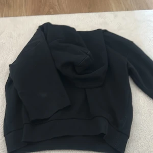 Svart hoodie med trekvarts ärm - Säljer en svart hoodie med klassisk huva och tre kvarts ärmar. Tröjan har ribbade muddar vid ärmslut och nederkant, vilket ger en snygg och bekväm passform. Perfekt för chill dagar eller när du vill ha en enkel och stilren look.