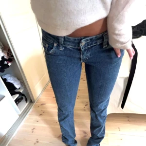 Blå jeans med döskallebroderi från Miss Me - Säljer ett par blå jeans från Miss Me med låg midja och straight fit. Baksidan har snygga fickor med broderad döskalle, vingar och krona samt pärldetaljer. Jeansen har klassisk femficksdesign och är gjorda i jeansmaterial med coola detaljer.