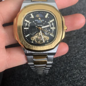 Herrklocka – replika, guld/silver, automatisk design - Stilren och elegant herrklocka i tvåfärgat stål (guld/silver) med en sportig men exklusiv känsla. Klockan har en genomskinlig urtavla som visar det automatiska urverket och ger ett modernt och unikt utseende.  ✨ Perfekt som accessoar både till vardags och fest. 👉 OBS! Detta är en replika, inte original.  Specifikationer: 	•	Färg: Guld/Silver 	•	Urverk: Automatisk look 	•	Armband: Stål, tvåfärgat 	•	Skick: Använd, men i bra skick 	•	Passar: Herr 