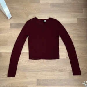Vinröd ribbad stickad tröja H&M - Snygg vinröd stickad tröja från H&M i storlek S. Tröjan är ribbad, har rund hals och är croppad med lång ärm. Perfekt för dig som gillar enkel stil med lite edge. Materialet är mjukt och skönt, passar till jeans eller kjol.