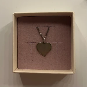 Silverfärgat halsband med hjärthänge - Snyggt halsband i silverfärg med ett stilrent hjärthänge. Kedjan är tvinnad och ger ett modernt intryck. Perfekt accessoar för att lyfta din outfit med en söt detalj.