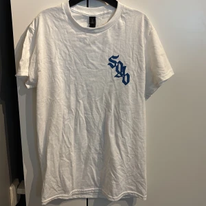Vit t-shirt Soppgirobygget - Vit t-shirt från Soppgirobygget med blått tryck fram och stort svampmotiv på ryggen. T-shirten har klassisk passform, rund hals och korta armar. Köpt på Brännbrollyran 2025. Men storleken var för liten. 