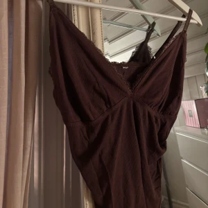 Brun ribbad linnetopp med spets - Säljer en brun linnetopp med ribbad struktur och tunna axelband. Toppen har v-ringad hals och fina spetsdetaljer längs kanten. Lapparna avklippta! Därför står det inte vart den är ifrån eller storlek, men skulle tippa på att den är ifrån Lindex. Passar mig i storlek XS/S. Är även väldigt töjbar i midjan.