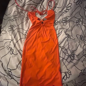 Orange omlottklänning Gina Tricot XXS - Snygg orange klänning från Gina Tricot i storlek XXS. Modellen är kort med omlottdetaljer och snörning framtill, samt tunna axelband som knyts i nacken. Materialet är mjukt och stretchigt, perfekt för dig som gillar färgstarka och trendiga plagg.