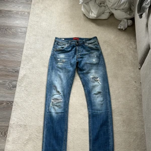 Slim Glenn jeans från Jack & Jones - Snygga blå jeans från Jack & Jones, modell Slim Glenn storlek 30/34 De har en slim passform och är tillverkade i klassiskt jeanstyg med slitna detaljer och hål på framsidan för en cool, avslappnad look. Flera fickor både fram och bak, samt bruna läderdetaljer vid linningen.priset kan diskuteras.