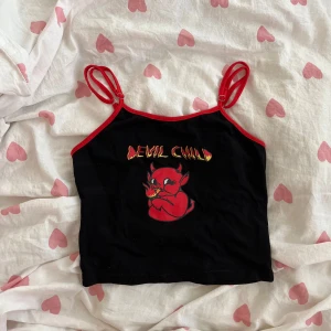 Svart croppad linnetopp - Svart croppad linnetopp med röda kantband och smala axelband. Framsidan har ett tryck med texten 'Devil Child' och en röd tecknad djävul!💞
