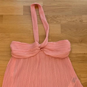 Plisserad rosa blus/topp med halterneck - Säljer en superfin plisserad ljusrosa blus/topp med halterneck och twistad detalj framtill,  har ett flowigt fall. Ny och har aldrig används. 