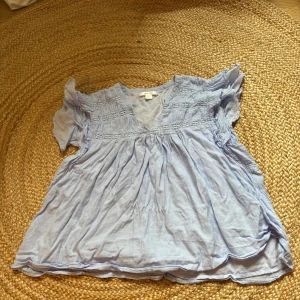 Ljusblå blus med volang från Gina Tricot - Supersöt ljusblå blus från Gina Tricot i storlek 158/164. Blusen har korta ärmar med volangdetaljer och v-ringad hals. Smockade partier upptill ger en chill och flowy känsla. Perfekt för vår och sommar när du vill ha en luftig och snygg look. Pris går att diskutera 💗💗