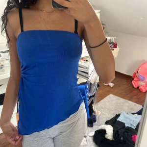 Blå linnetopp med snörning i sidan - Snygg blå linnetopp med smala axelband och cool snörningsdetalj i sidan som skapar en öppen effekt. Toppen har en asymmetrisk nederkant och är gjord i ett mjukt, stretchigt material som sitter skönt mot kroppen. Har inte använt den en ända gång så den är som ny 