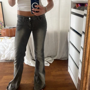 Grå bootcut jeans med låg midja - Säljer ett par grå jeans med snygg faded effekt och bootcut passform. De har låg midja, klassiska fem fickor och dragkedja med knapp. Materialet är jeans och de sitter riktigt bra över höfterna. Perfekt för dig som gillar en cool och avslappnad stil. Finns slitage vid hällarna då de var lite för långa för mig 