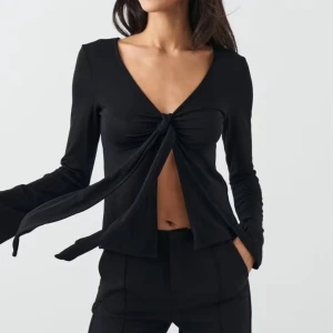 Svart omlottopp med knyt från Gina Tricot - Svart långärmad omlottopp från Gina Tricot i storlek XS. Toppen har djup v-ringning och snygg knytning framtill som ger en öppen look över magen. Första 2 bilderna är från Gina tricots hemsida