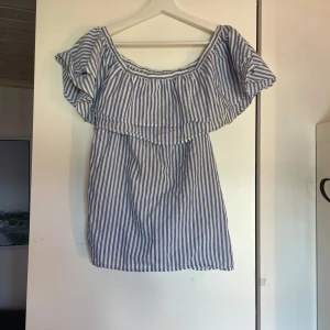 Randig topp Gina Tricot - Säljer en söt blåvit randig topp från Gina Tricot i storlek 34. Toppen har volang runt axlarna och är tillverkad i mjuk bomull, perfekt för varma dagar.