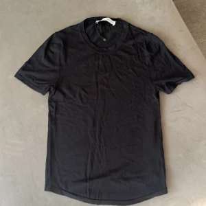 Svart t-shirt från Zara, storlek M - Svart finstickad t-shirt från Zara i storlek M. Modellen har rund hals och korta ärmar, perfekt för en clean och enkel look. Materialet är mjukt och känns skönt mot huden, troligtvis bomull. Passformen är normal och t-shirten är helt enfärgad utan mönster eller detaljer.