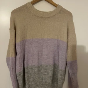 Pigalle/only stickad tröja  - Säljer en chill stickad tröja från Pigalle i storlek M. Tröjan har breda blockränder i beige, ljuslila och grått, med rund hals och långa ärmar. Perfekt för dig som gillar mjuka färger och vill ha en mysig look. 