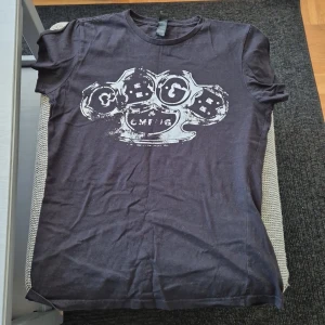 Svart t-shirt med tryck från CMFJ - Cool svart t-shirt från CMFJ med ett stort vitt tryck av en knogjärnsdesign på bröstet. Klassisk rund hals och korta ärmar. Perfekt för dig som gillar streetstyle och vill sticka ut med en unik grafisk detalj.