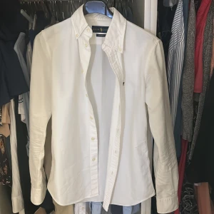 Vit skjorta från Ralph Lauren XS - Vit skjorta från Ralph Lauren i bomull, custom fit. Klassisk button-down krage, långärmad och med knappar framtill. Diskret broderad logga på bröstet. Perfekt för dig som gillar stilrena och tidlösa plagg.