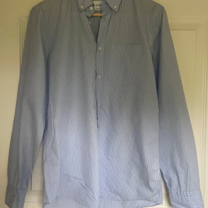 Blå randig skjorta från Dondup - Snygg blå skjorta från Dondup med vita ränder och en klassisk krage och knappstängning. Den är tillverkad i mjuk bomull. Vid frågor och funderingar är de bara att höra av sig. Inga byten!!!