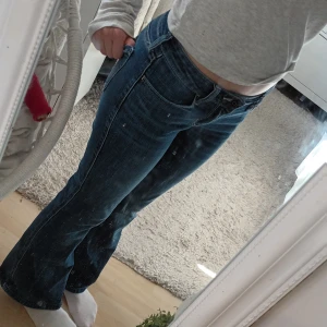 Blå bootcut jeans från Hollister - Säljer ett par snygga blå jeans från Hollister med bootcut passform och låg midja. Jeansen har klassisk femficksdesign, bälteshällor och dragkedja med knapp. Materialet är mjukt denim i bomull med lite stretch för extra komfort.