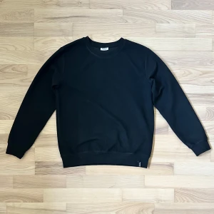 Svart ribbad tröja från Kappahl - Svart långärmad tröja från Kappahl i storlek 159/164. Tröjan har en ribbad struktur och rund halsringning, med klassisk passform och mjuka muddar vid ärmslut och nederkant. Perfekt för dig som gillar enkel och stilren look.