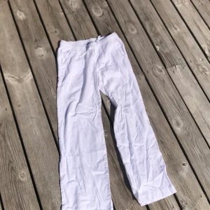 Vita linnebyxor från 157, storlek 150 - Snygga vita linnebyxor från 157 med elastisk midja och snörning. Byxorna har raka ben, sidofickor fram och en bakficka. Perfekta för chill dagar och sommarhäng, riktigt sköna och luftiga. Passar dig som gillar enkel och clean stil.