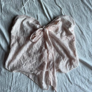 Rosa tubetopp - Supersöt ljusrosa tubtopp med spets och en stor rosett framtill som man även kan knytta om eller ta bort helt. Det finns en ”rem” över nacken som man kan klippa bort, den sitter likadant oavsett om man har bandet kvar eller inte :)) aldrig använt !!den är mer baby rosa i verkligheten!!