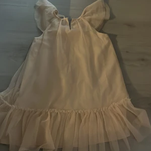 Champagnefärgad volangklänning H&M - Säljer en söt champagnefärgad kortklänning från H&M med volangkant nedtill och luftiga, korta ärmar. Klänningen har en lätt glittrig yta och är tillverkad i ett tunt, syntetiskt material som ger ett skirt och festligt intryck. Perfekt för dig som gillar romantisk stil.