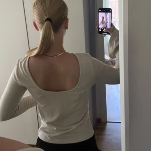 Beige långärmad topp från NA-KD - Snygg beige långärmad topp från NA-KD med rundad hals och djup, öppen rygg. Ärmarna är utsvängda. 