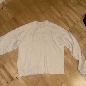 Vit stickad tröja med ribbade detaljer - Mysig vit stickad tröja med ribbad hals, ärmslut och nederkant. Tröjan har en relaxed passform och är perfekt för kyliga dagar. Enkel och stilren design som funkar till många outfits.