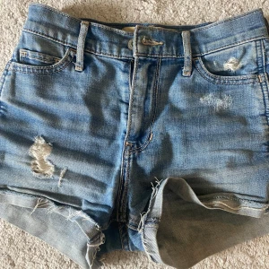 Högmidjade jeansshorts från Hollister - Snygga ljusblå jeansshorts från Hollister med hög midja och råa, fransiga benslut. Shortsen har slitna detaljer både fram och bak samt klassiska fickor. Säljer för att dom är för små 💕