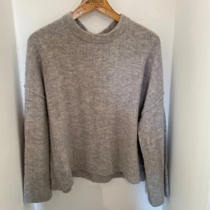 Grå stickad tröja med rund hals - Mysig grå stickad tröja med rund hals och långa ärmar. Tröjan har en enkel, loose passform och diskreta vertikala ränder i stickningen. Perfekt för kallare dagar💕