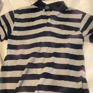 Randig Polo t-shirt från Ralph Lauren - Jag säljer den för den är för liten för mig och jag är inte 170cmSnygg randig t-shirt från Polo Ralph Lauren i marinblått och grått. Klassisk pikékrage, två knappar och ikonisk röd broderad logga på bröstet. Tillverkad i 100% bomull för skön känsla. Perfekt för chill och stilren look. 