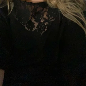 Svart blus med spets från VILA - Svart blus från VILA med lång ärm och snygg spetsdetalj över bröstet och axlarna. Blusen har en liten volang vid halsen och ett blommigt spetsmönster! Köparen står för frakt! ❣️