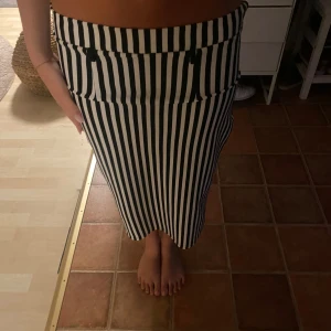 Svartvit randig midikjol - Snygg svartvit randig kjol med raka vertikala ränder och midilängd. Kjolen har en figurnära passform och bred linning. Perfekt för dig som gillar en stilren och trendig look.